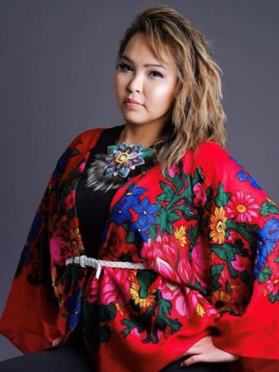 A woman posing wearing a bright red floral top